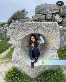 A white female with long brown hair smiles at the camera crouched inside a large stone carving. 